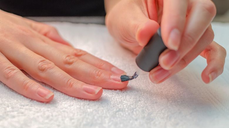 someone applying a base coat to prepared nails before starting nail art